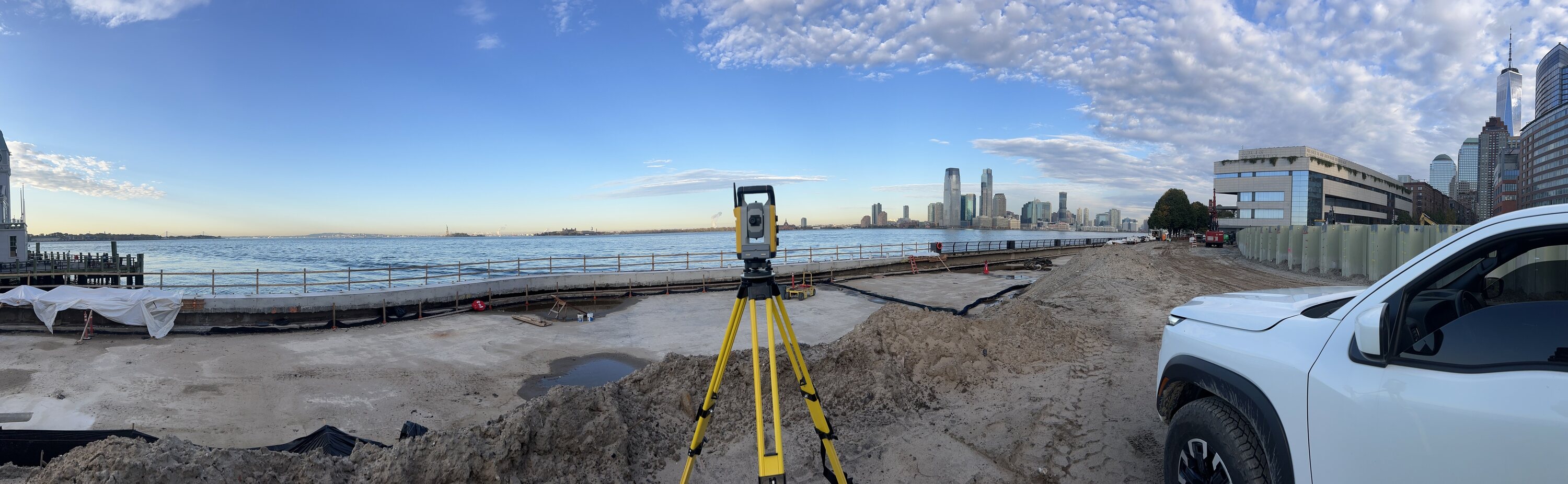 Panoramic view from Battery Park City showing Trimble total station with the Statue of Liberty, Jersey City skyline, and One World Trade Center